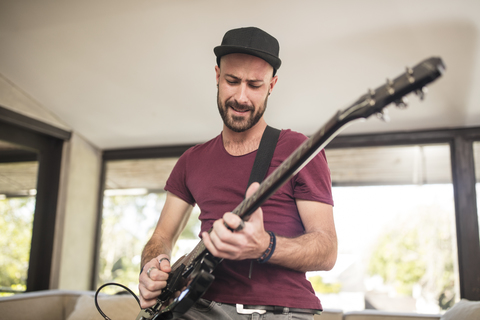 Leidenschaftlicher junger Mann spielt E-Gitarre im heimischen Wohnzimmer, lizenzfreies Stockfoto