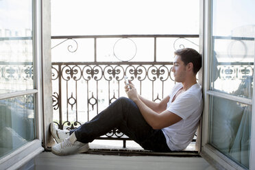 Man using cell phone in windowsill - CUF40702