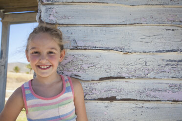 Portrait of girl wearing striped vest by clapboard cabin - CUF40794