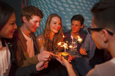 Gruppe von Teenagern, die um einen Geburtstagskuchen mit Wunderkerzen sitzen - CUF40804