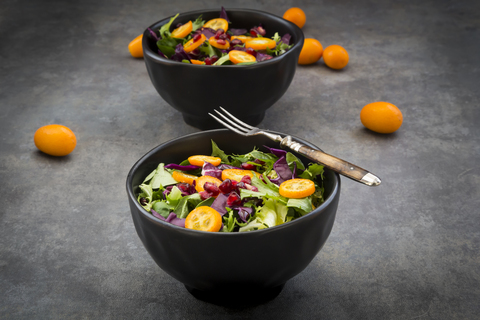 Bowl of mixed green salad with red cabbage, kumquat and pomegranate seeds stock photo