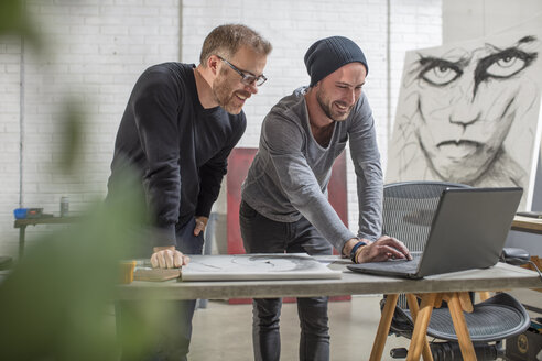 Lächelnder Künstler mit Laptop und Mann im Atelier - ZEF15877