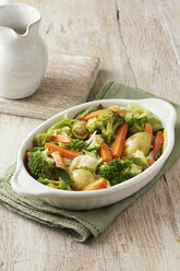 Gemüseauswahl bestehend aus Brokkoli, Karotten, neuen Kartoffeln und Kohl in weißer Servierplatte auf grünem Tuch - CUF41179