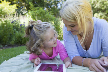Mutter und Tochter liegen auf einer Decke im Garten und benutzen ein digitales Tablet - CUF41298