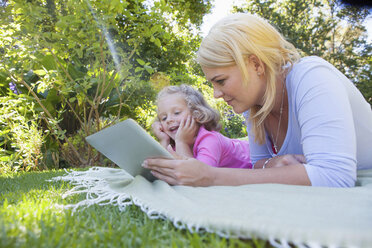 Mutter und Tochter liegen auf einer Decke im Garten und benutzen ein digitales Tablet - CUF41299