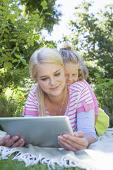Mother and daughter lying on blanket in garden using digital tablet - CUF41302