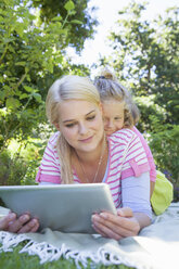 Mutter und Tochter liegen auf einer Decke im Garten und benutzen ein digitales Tablet - CUF41302