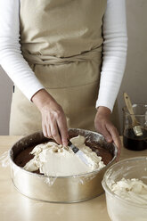 Frau bei der Zubereitung eines Schokoladenkuchens, Verteilen von Sahne - CUF41312