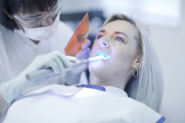 Female dentist using ultraviolet light on patients teeth - CUF41542