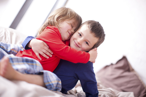 Zwei kleine Kinder umarmen sich auf dem Bett, lizenzfreies Stockfoto