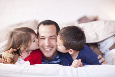 Sohn und Tochter küssen Vaters Wange unter der Bettdecke - CUF41555