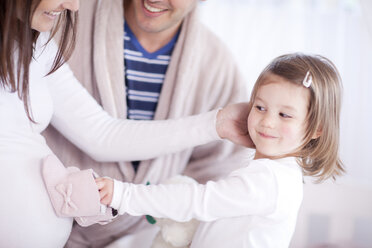 Young daughter holding baby booties on mothers bump - CUF41557