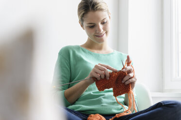 Young woman sitting in window seat knitting - CUF41588