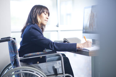 Woman in wheelchair writing notes - CUF41682