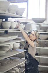 Potter stacking bowls onto shelf at crockery factory - CUF41746