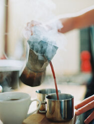 A person holding a coffee percolator and pouring hot coffee into cups. - MINF00001