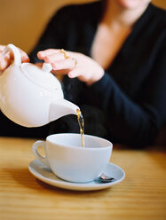 Eine sitzende Frau gießt eine Tasse Tee aus einer weißen Porzellankanne ein. - MINF00003