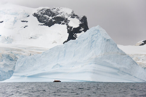 Menschen in kleinen aufblasbaren Zodiac-Rippenbooten passieren Eisberge und Eisschollen auf dem ruhigen Wasser um kleine Inseln in der Antarktis. - MINF00012