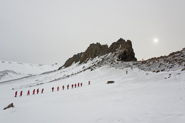 Reisende in leuchtend orangefarbenen Regenjacken laufen in einer Reihe durch den Schnee auf Deception Island. - MINF00014