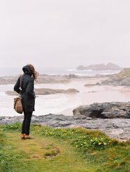 Eine Frau blickt an einem windigen Tag am Meer über die Felsen und das Ufer. - MINF00019