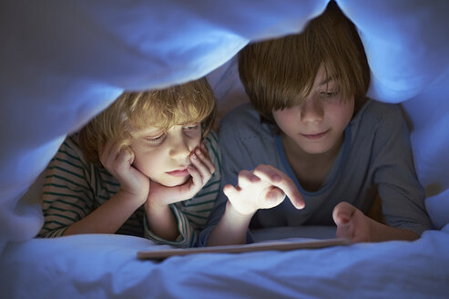 Brothers underneath duvet using digital tablet - CUF41964