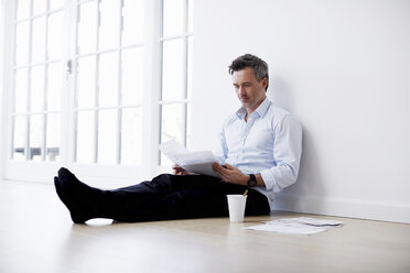 Man sitting on floor looking at paperwork - CUF41967