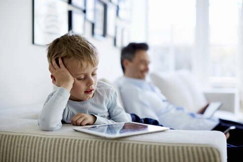 Father and son sitting on sofa using digital tablets - CUF41968