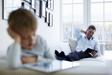 Father and son sitting on sofa using digital tablets - CUF41969