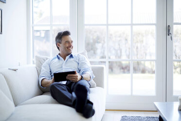 Man relaxing on sofa using digital tablet - CUF41970