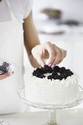 Frau dekoriert Torte mit frischen Brombeeren - CUF42035