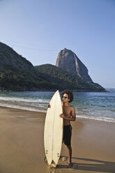 Mann hält Surfbrett am Strand, Rio de Janeiro, Brasilien - CUF42251