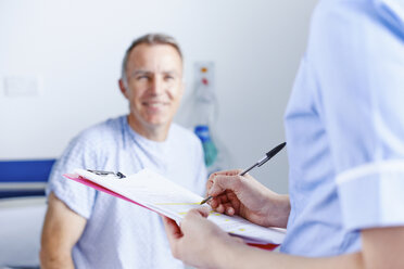 Krankenschwester beim Erledigen von Papierkram, Patient im Hintergrund - CUF42571
