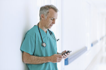 Chirurg steht im Korridor und schaut auf sein Smartphone - CUF42573