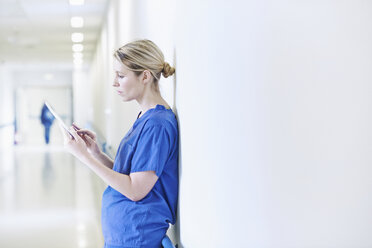 Arzt steht im Korridor und schaut auf ein digitales Tablet - CUF42575