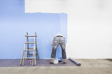 Rear view of man painting wall blue - CUF42654
