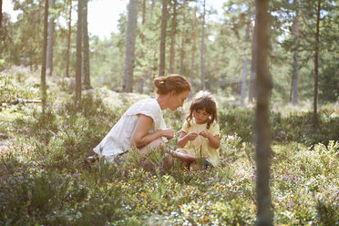 Mutter und Tochter sitzen im hohen Gras und betrachten die Pflanzen - CUF42686