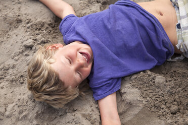 Boy lying on sand laughing, Wales, UK - CUF42717