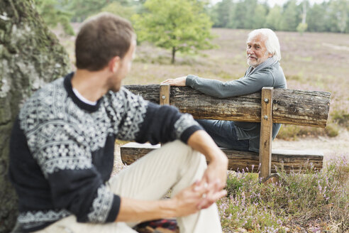 Älterer Mann sitzt auf einer Bank und unterhält sich mit einem mittelalten Mann - CUF42769