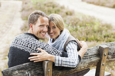 Mid adult couple on wooden bench looking at camera - CUF42771