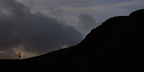 Junger Mann läuft auf einen Berg mit Silhouette - CUF42778