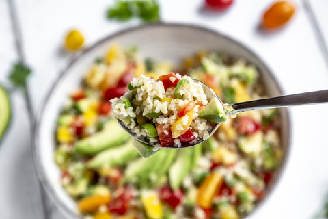 Spoon of bulgur salad with bell pepper, tomatoes, avocado, spring onion and parsley stock photo