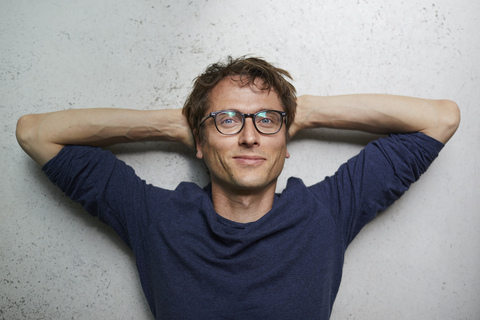 Portrait of smiling man with hands behind head wearing glasses stock photo