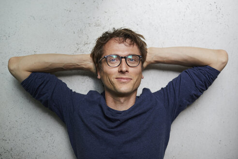 Portrait of smiling man with hands behind head wearing glasses - PNEF00751