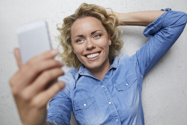 Porträt einer lächelnden blonden Frau, die ein Selfie mit ihrem Smartphone macht - PNEF00754