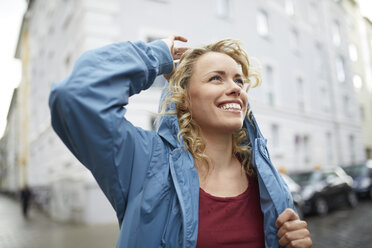 Portrait of smiling blond woman putting on her hood - PNEF00759