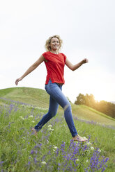 Portrait of happy blond woman running barefoot on a meadow - PNEF00760