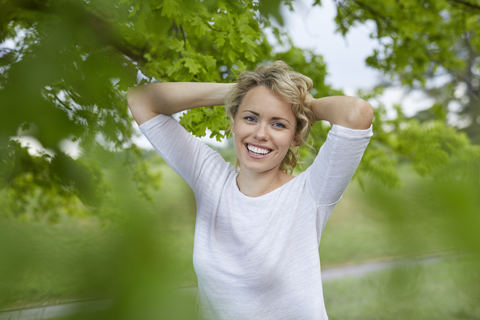 Porträt einer entspannten blonden Frau mit den Händen hinter dem Kopf in der Natur, lizenzfreies Stockfoto