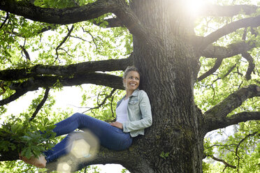 Smiling woman sitting on branch relaxing - PNEF00768