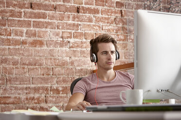 Young man using computer wearing headphones - CUF42899