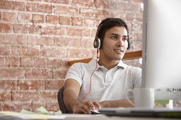 Young man using computer wearing headphones - CUF42900